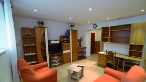 Ein Wohnzimmer mit zwei orangenen Sofas, einem Couchtisch, einem Fernseher und integrierten Holzregalen.