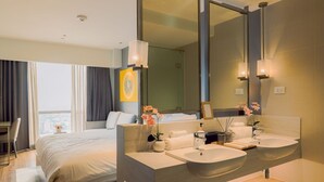 Een hotelkamer met een groot bed, twee wastafels, een spiegel en uitzicht op de stad.
