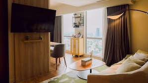 Un saló modern amb televisió de pantalla plana, un sofà, una taula de centre, una zona de menjador amb una cadira i vista a la ciutat a través de grans finestres.