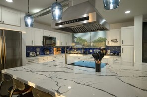 A modern kitchen with white cabinets, a marble island, stainless steel appliances, and blue hexagonal backsplash tiles. -  Luxury Waterfront Home,Sleeps 20, Pool, Hot Tub, Fishing Pier, Basketball Court (Rio Hondo)