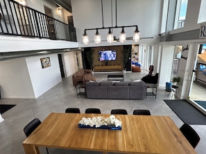 A spacious living area with a large sofa set, a wooden dining table with a floral centerpiece, and a television mounted on the wall. -  Luxury Waterfront Home,Sleeps 20, Pool, Hot Tub, Fishing Pier, Basketball Court (Rio Hondo)