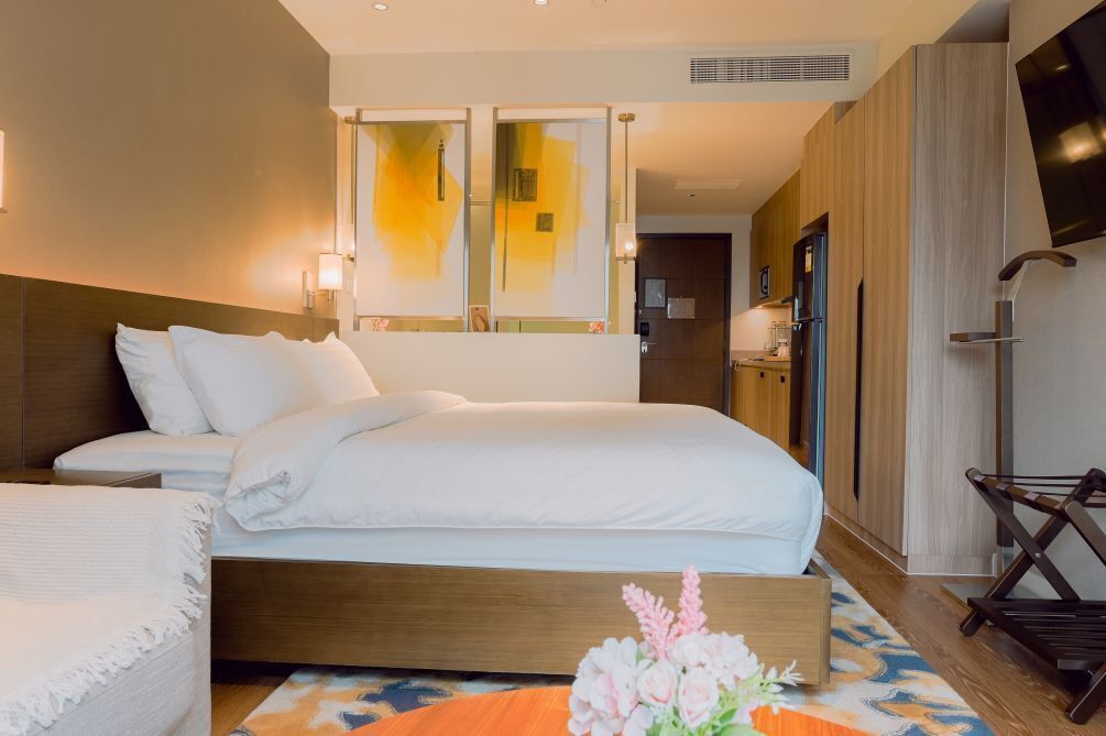 A hotel room with a bed, bedside table, and a small seating area with a chair.