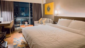 A hotel room with a large bed, a desk, a chair, a sofa, and a view of the cityscape. - Cozy Private Room w King (Mandaluyong City)
