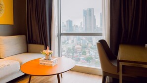 A modern living room with a sofa, a round coffee table with books, a chair, and a large window with a city view. - Sunset Serenity King Suite (Mandaluyong City)