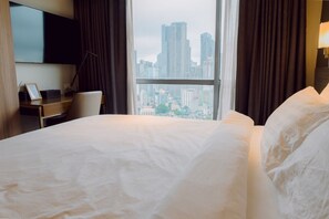 A hotel room with a bed, a desk, a chair, a TV, and a window with a city view. - Sky High Serenity w King (Mandaluyong City)