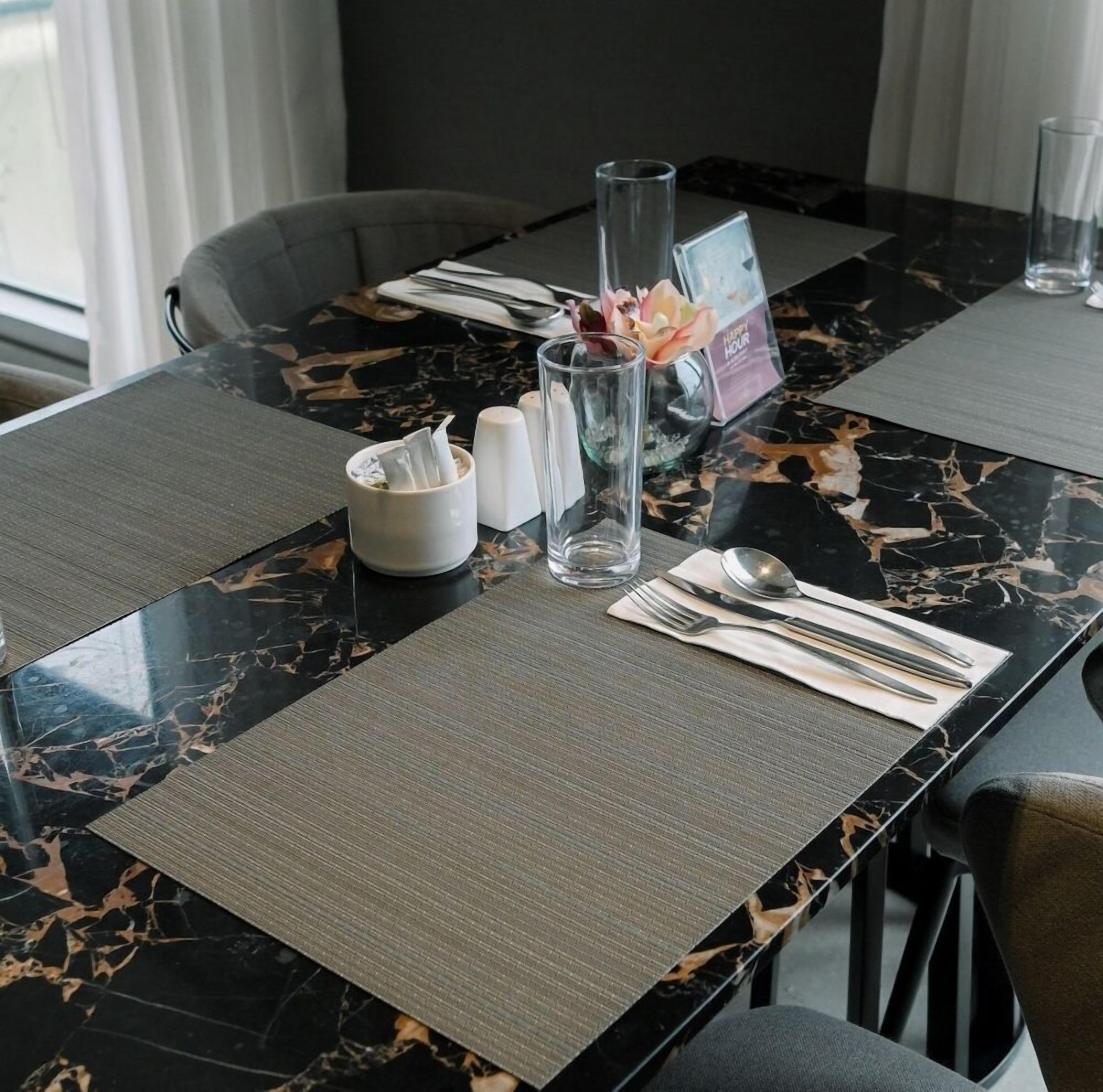 A dining table with a marble top, a placemat, a glass vase with flowers, a menu, and cutlery.