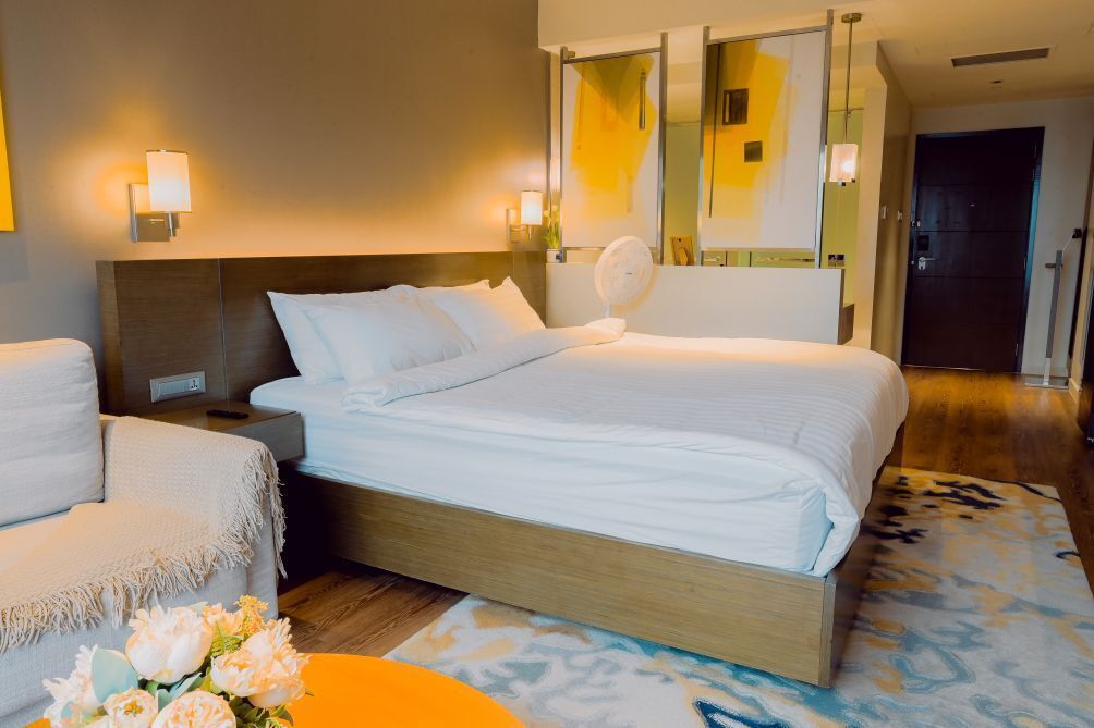 Et hotelværelse med seng, sengeborde, en stol, et spejl og en ventilator fastgjort på væggen.