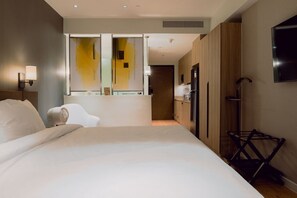 A modern hotel room with a large bed, a wall-mounted TV, a small kitchenette, and a walk-in closet. - Chic Riverfront Escape at Acqua (Mandaluyong City)
