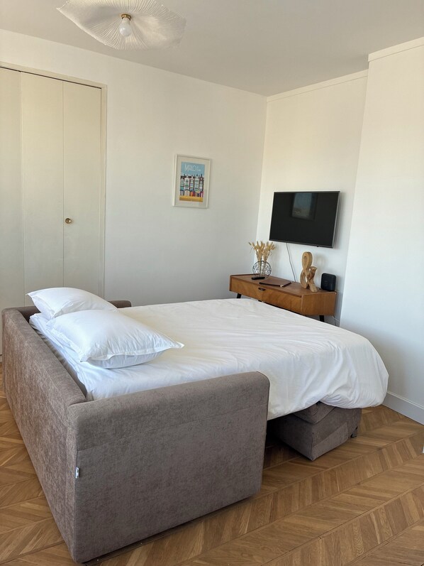 A bedroom with a bed, a wardrobe, a television, and a small wooden side table.