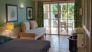 Een slaapkamer met een bed, een bank, een klein tafeltje en een balkon met uitzicht op groen.