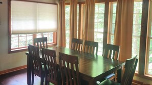 A dining area with a wooden table and chairs, large windows with curtains, and a ceiling with exposed beams. - Creekside serenity in murphy (Murphy)
