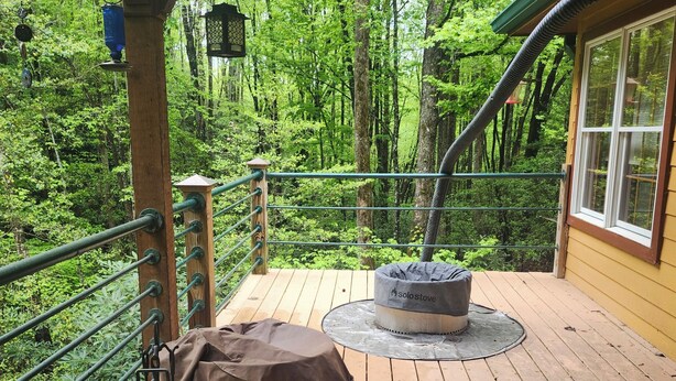 A wooden deck with a metal railing, a covered seating area, and a portable stove. - Creekside serenity in murphy (Murphy)