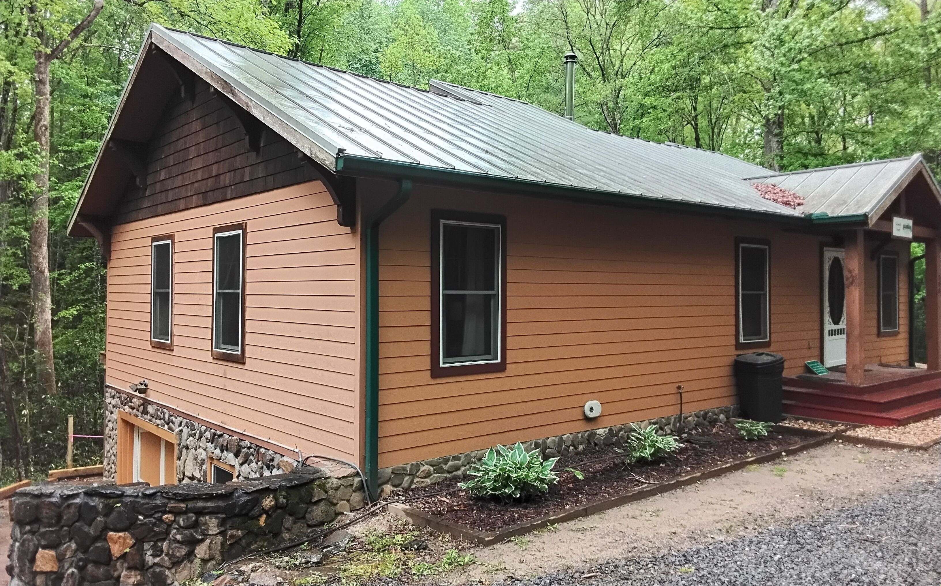 Eine Holzhütte mit Steinunterbau, einem Metalldach und einer kleinen Veranda.