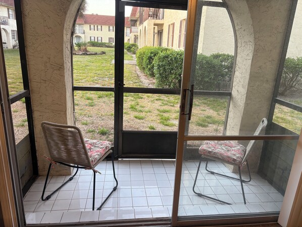 A room with a glass door leading to a balcony, two wicker chairs, and a tiled floor. - 2-bedroom condo on beach Blv by Jaguar Stadium with two pools (Jacksonville)