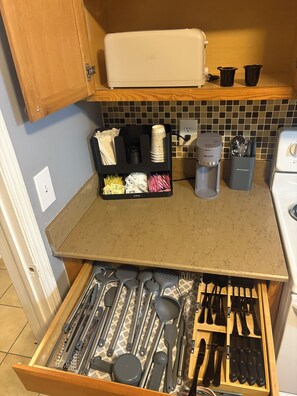 A kitchen with a drawer organizer holding various utensils, a coffee maker, and a trash bin. - 2-bedroom condo on beach Blv by Jaguar Stadium with two pools (Jacksonville)