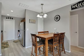 A dining area with a wooden table and chairs, a chandelier, a clock, and a welcome sign. - The Chardonnay - Wine Down at our Cozy 3BR Getaway in Branson (Branson)