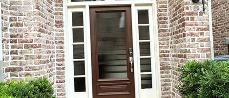 A brick house with a brown front door, a small porch, and a doormat with 'HOME' written on it.