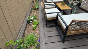 En træterrasse med udendørs møbler, grill og krukker med planter.
