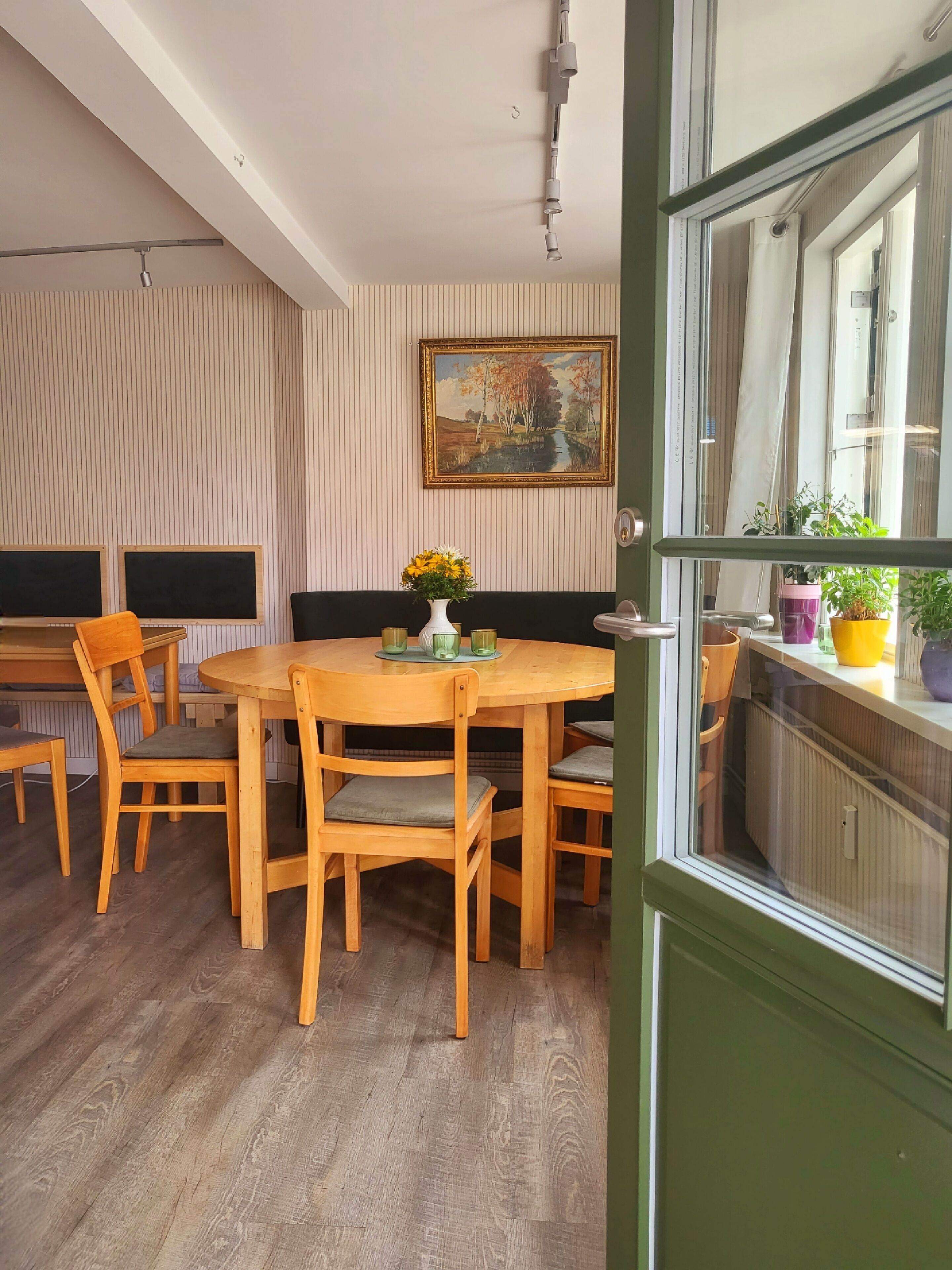 Un coin repas avec une table ronde en bois, quatre chaises, un vase de fleurs et un tableau accroché au mur.