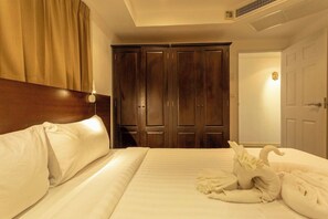 A hotel room with a large bed, a wooden wardrobe, and a door with a light fixture. - Famous Kata Ocean View 2BR Seaview Residence c129 (Tambon karon)