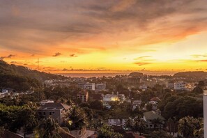 A coastal town at sunset with buildings and palm trees. - Famous Kata Ocean View 2BR Seaview Residence c129 (Tambon karon)
