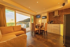 A modern hotel room with a sofa, dining table, chairs, a kitchen area, and a TV. - Famous Kata Ocean View 2BR Seaview Residence c129 (Tambon karon)