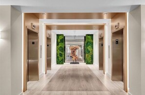 Ein moderner Aufzugsbereich mit einer zentralen Kunstinstallation, zwei Aufzügen und Holzboden.