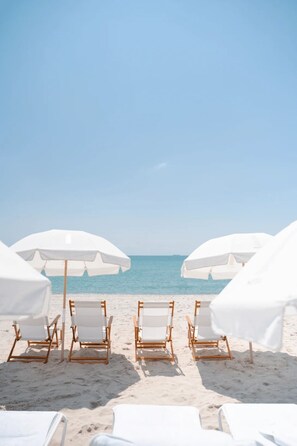 Ein Strand mit weißen Sonnenschirmen und Holzliegen.