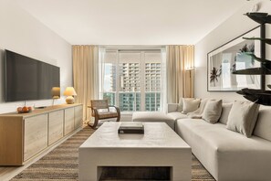 Ein modernes Wohnzimmer mit Flachbildfernseher, einer Couch, einem Couchtisch, einem Bücherregal und einem großen Fenster mit Blick auf die Stadt.