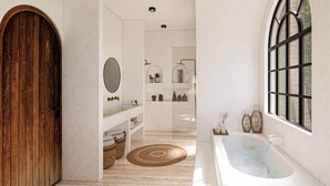 Ein modernes Badezimmer mit Holztür, großem Spiegel, einer Badewanne, Ablagen mit Toilettenartikeln und einem Fenster mit Aussicht.