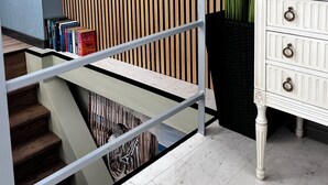 A staircase with a metal railing, a wooden slatted wall, a white dresser with drawers, and a bookshelf with books. - Sea Loft Varna - Entire 3-level 125sq.m. house in the top historical center (Varna)