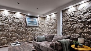 A cozy living room with a stone wall, a cushioned sofa, a wooden coffee table, and a small side table with a lamp. - Sea Loft Varna - Entire 3-level 125sq.m. house in the top historical center (Varna)