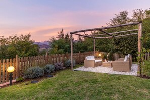A wooden pergola with wicker furniture, a gravel area, and a wooden fence. - Farmhouse in Tuscany With Pool and Scenic Views (Lucca)