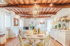 A dining area with a round table, chairs, a chandelier, and a white cabinet with decorative items. - Farmhouse in Tuscany With Pool and Scenic Views (Lucca)