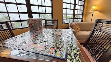 A puzzle on a glass table in a room with large windows, a sofa, and a lamp.