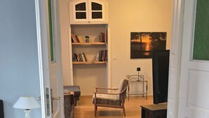 Een open doorgang naar een woonkamer met een boekenkast, een stoel, een kleine tafel en een televisie.
