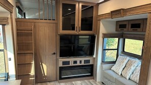 A compact RV interior with a kitchenette, a seating area with a window, and a TV mounted on the wall. - Unique Country Getaway Luxury Peaceful & Spacious (Cleveland)