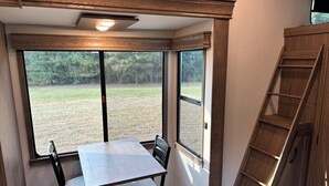A corner room with a dining table, two chairs, a window with a view of a grassy field, and a wooden ladder. - Unique Country Getaway Luxury Peaceful & Spacious (Cleveland)