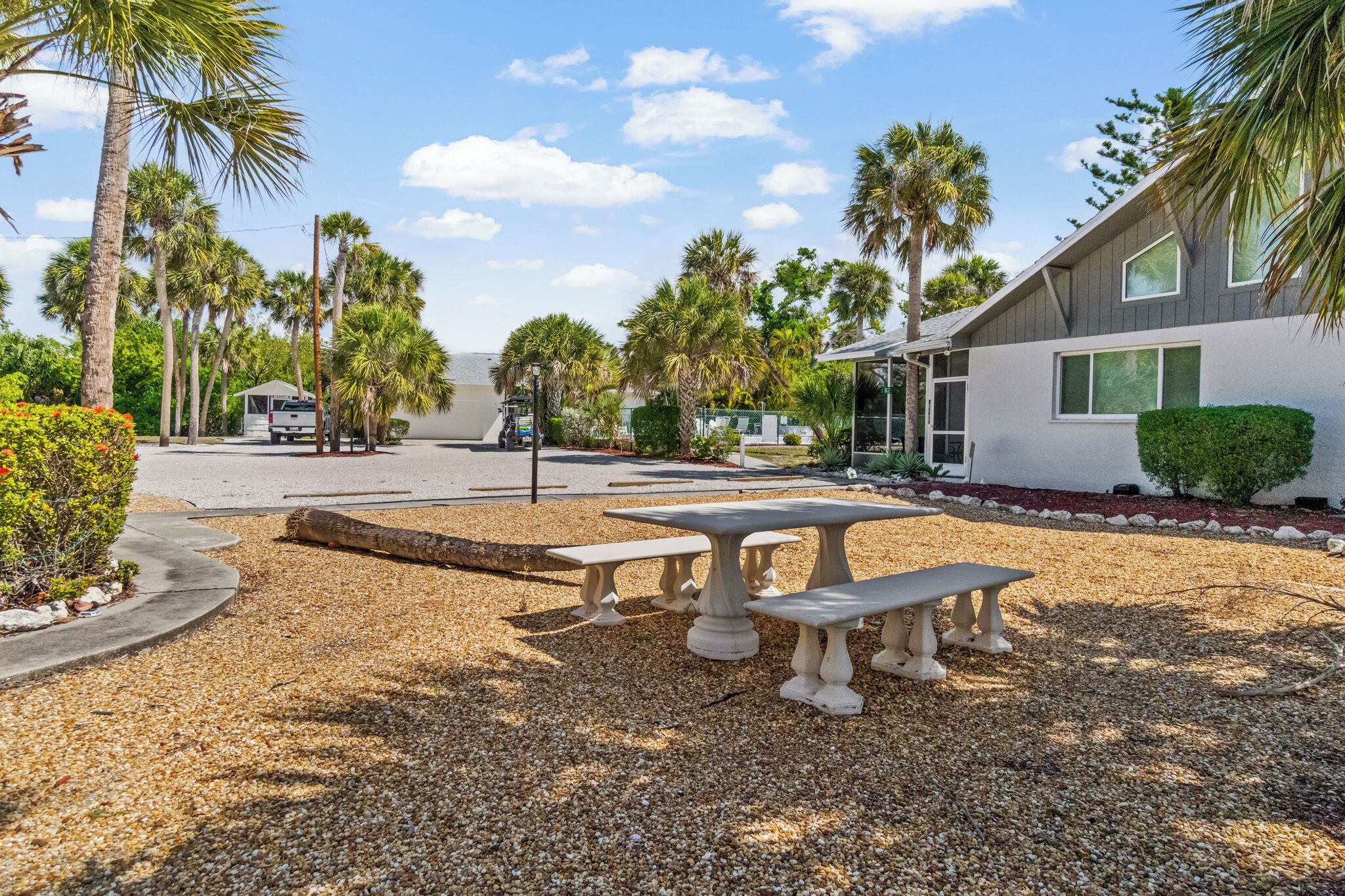 A gravel patio with outdoor tables and benches, palm trees, and a building with a modern design.