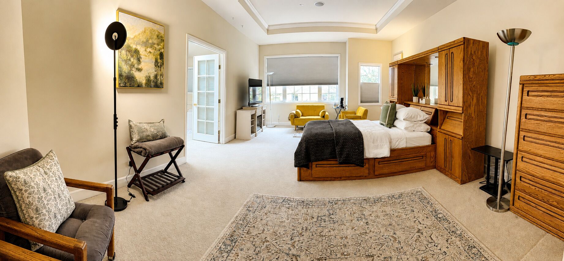 Une chambre à coucher comprenant un lit, un canapé, une chaise, une lampe sur pied, un bureau et une grande fenêtre.