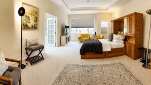 Een slaapkamer met een bed, een slaapbank, een stoel, een vloerlamp, een bureau en een groot raam.
