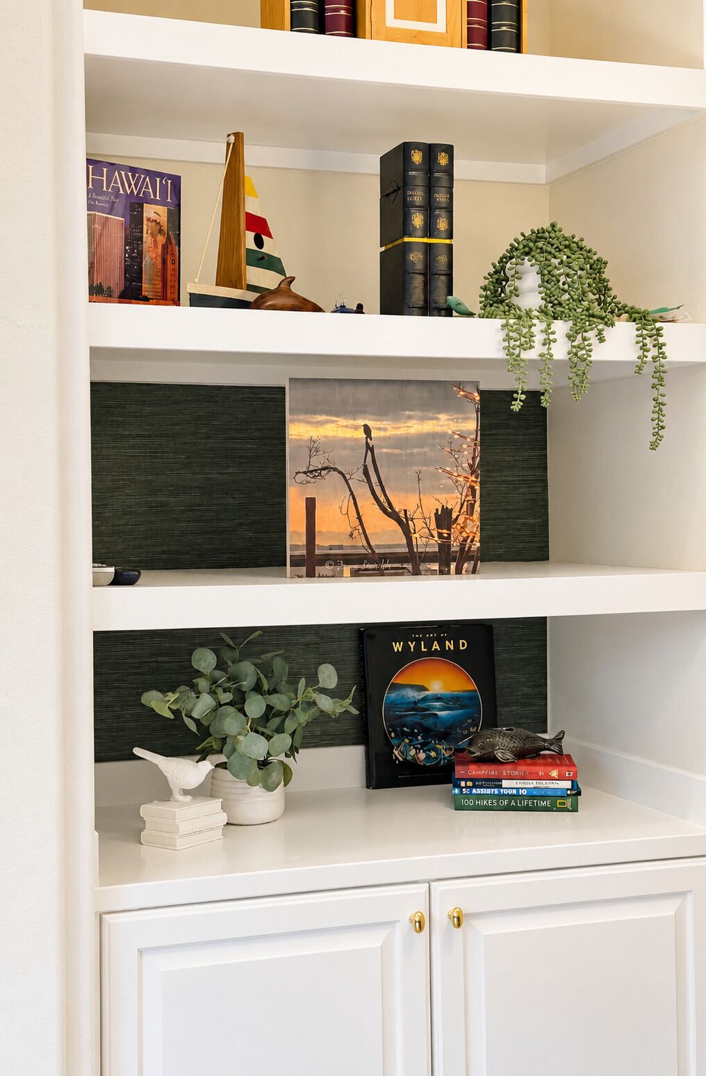 Une bibliothèque remplie de livres, un tableau encadré et quelques objets de décoration.
