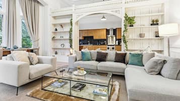 A modern living room with a glass coffee table, two sofas, and a view into the kitchen.