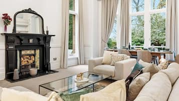 A living room with a fireplace, a sofa set, a coffee table, and large windows with curtains.
