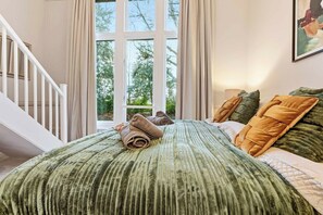 Une chambre avec une grande fenêtre, un lit avec une literie verte et un escalier.