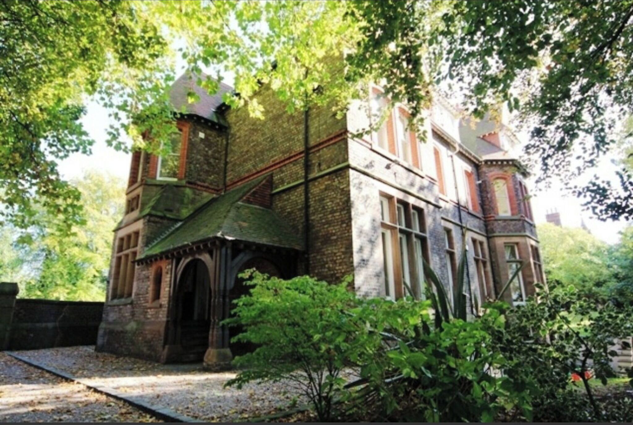 A historic building with a turret and arched entrance, surrounded by lush greenery.
