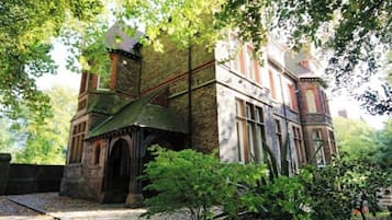A historic building with a turret and arched entrance, surrounded by lush greenery.