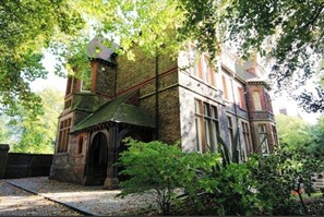 Un bâtiment historique doté d’une tourelle et d’une entrée en arc de cercle, entouré d’une végétation luxuriante.