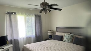 A bedroom with a bed, a ceiling fan, a television on a stand, and curtains. - Updated 1BR Across from Ocean – Prime Deerfield Beach Location (Deerfield Beach)