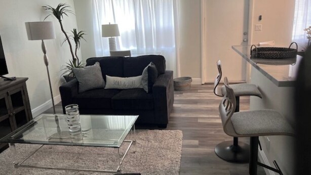 A living room with a sofa, a glass coffee table, a lamp, and a chair. - Updated 1BR Across from Ocean – Prime Deerfield Beach Location (Deerfield Beach)